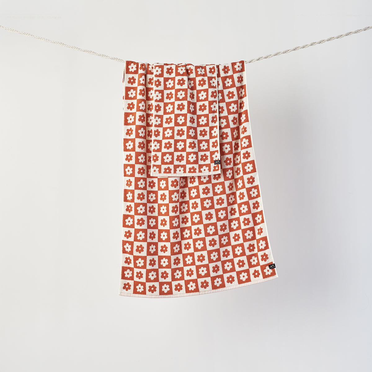 Towels, sustainably sourced cotton, red and white floral geometric pattern, hanging on line.