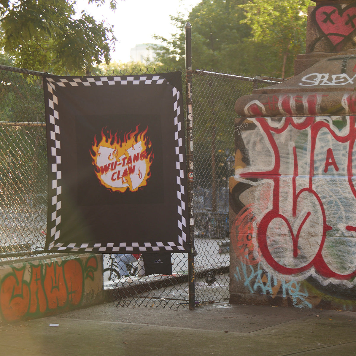 Picnic blanket with bold logo pattern, displayed outdoors on a chain-link fence.