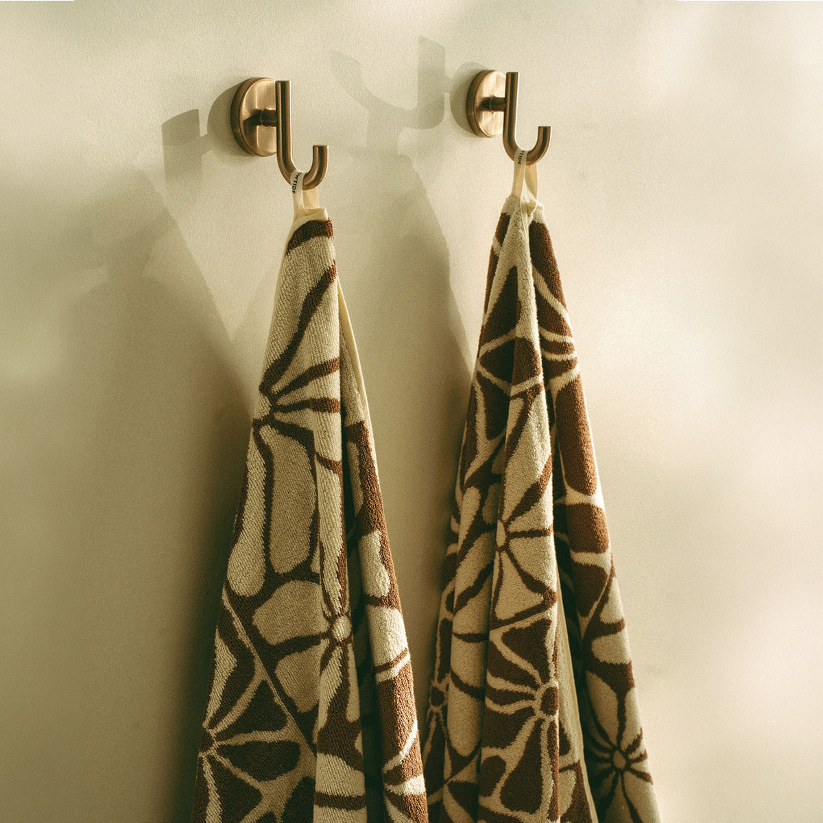 Geometric pattern towels hanging on brass wall hooks.