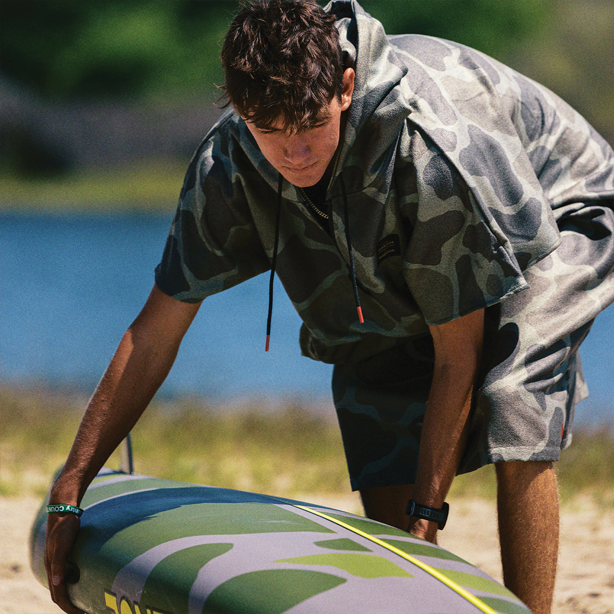 Camo surf changing poncho with hood, on sandy beach near water.