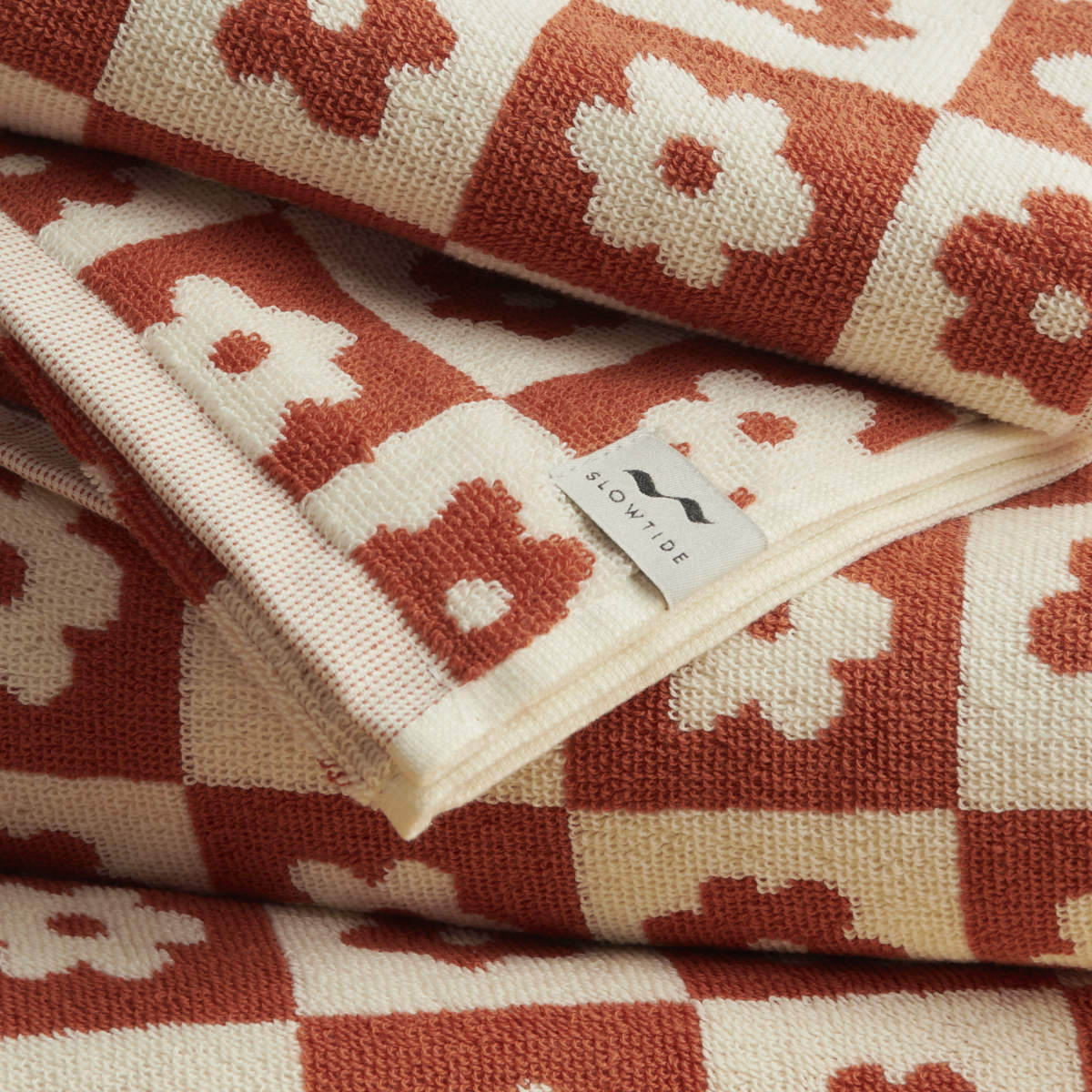 Towel with red and cream floral geometric checks, folded with fabric tag visible.