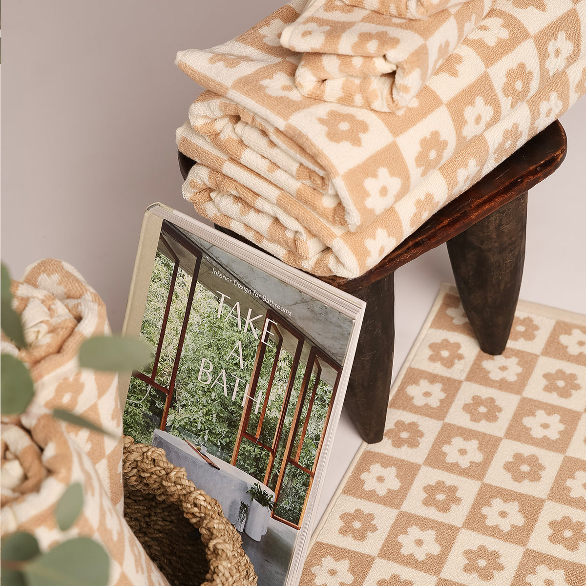 Beige floral checkerboard towel and matching mat set on wooden stool with woven basket.