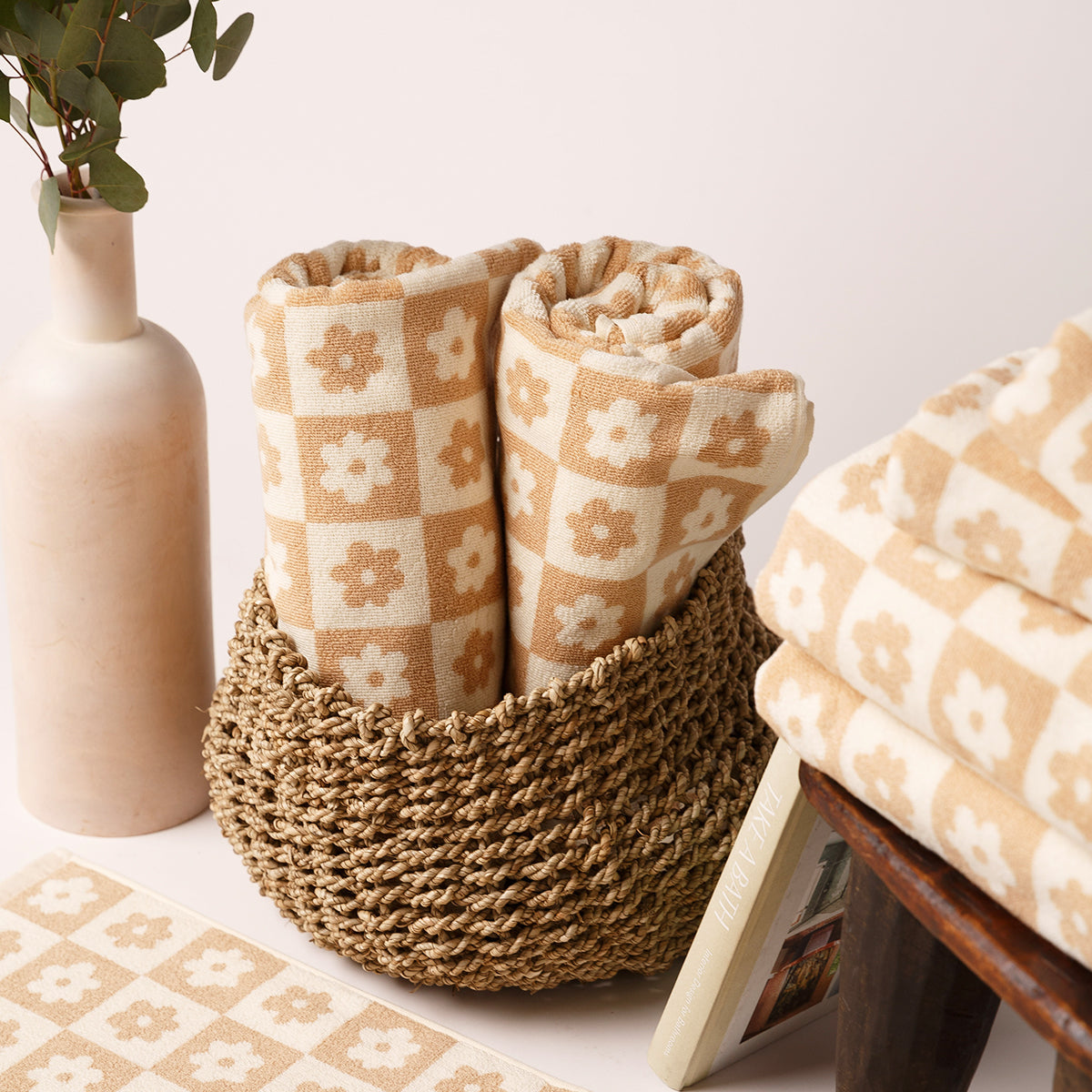 Cotton towels with beige floral checkerboard pattern rolled in a basket next to folded bath towels.