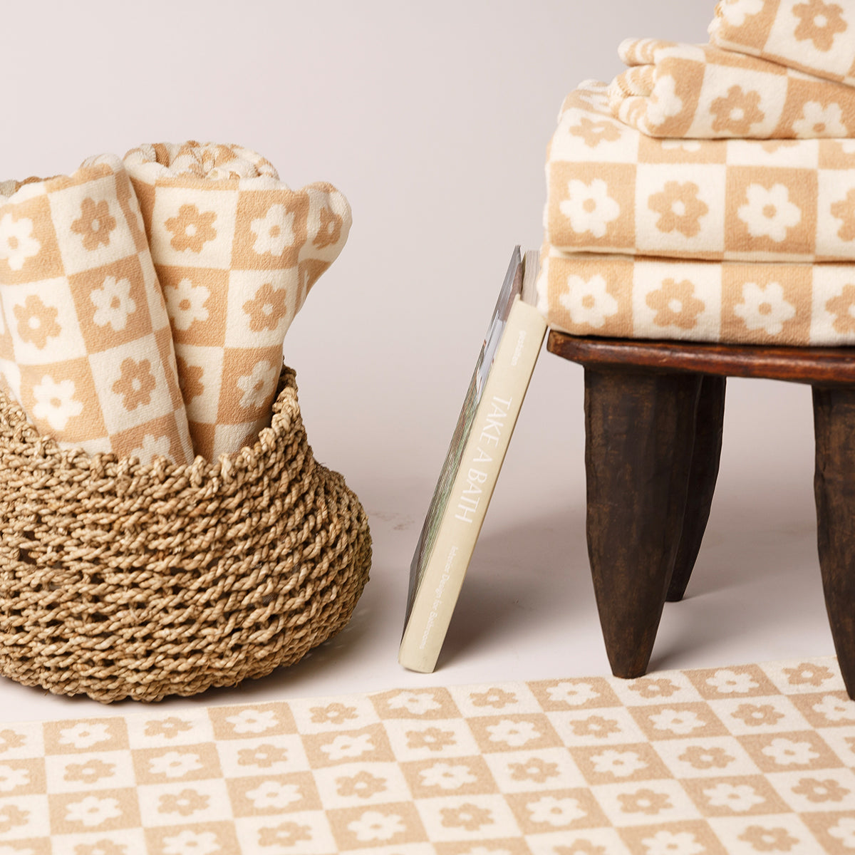 Cotton beige and white bath towels in a basket, on a stool, and laid out on the floor.