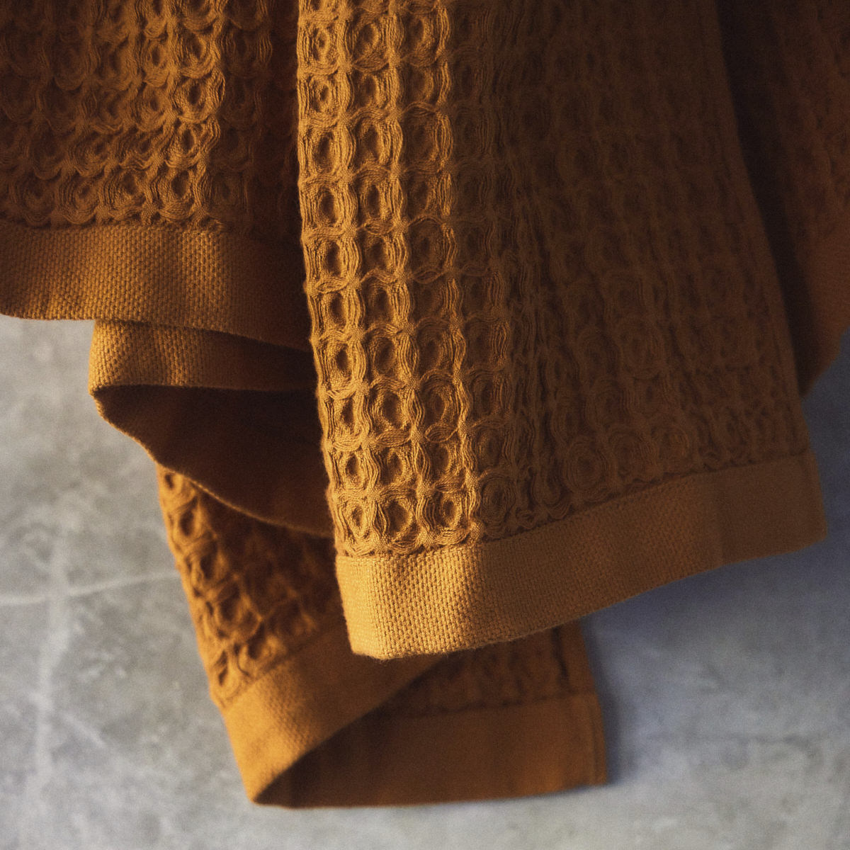 Waffle bath towel in textured orange cotton on a gray surface.