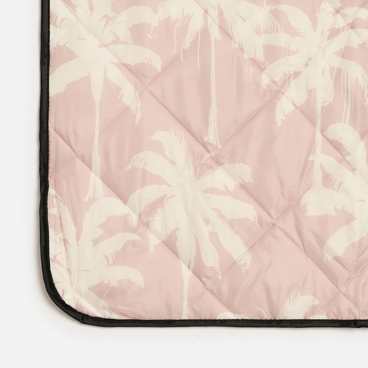 Quilted water-resistant blanket with white palm tree print, pale pink background, black trim.