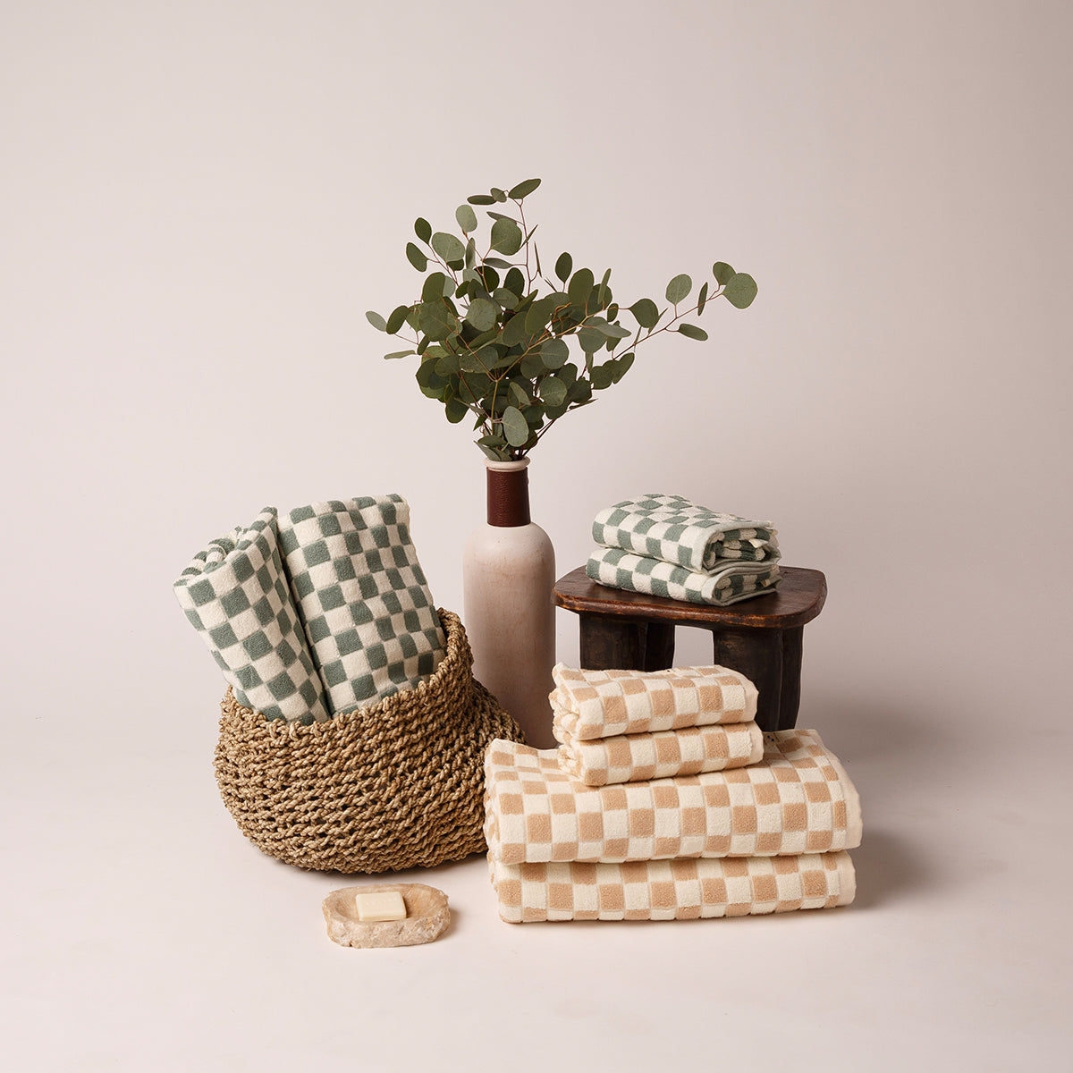 Sandstone towels stacked, woven basket beside vase with greenery on a neutral surface.