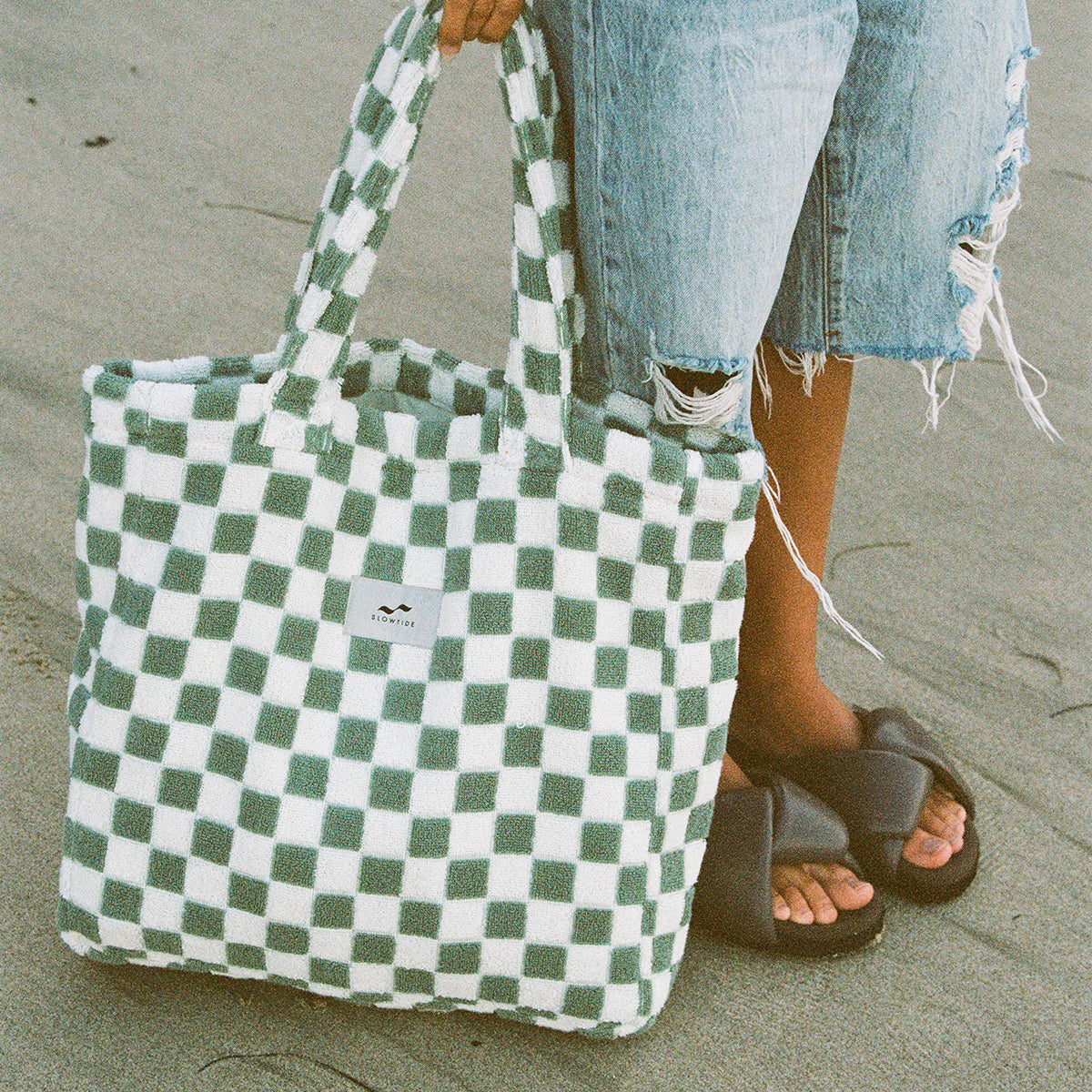 Checker pattern tote bag with green and white design on sand.