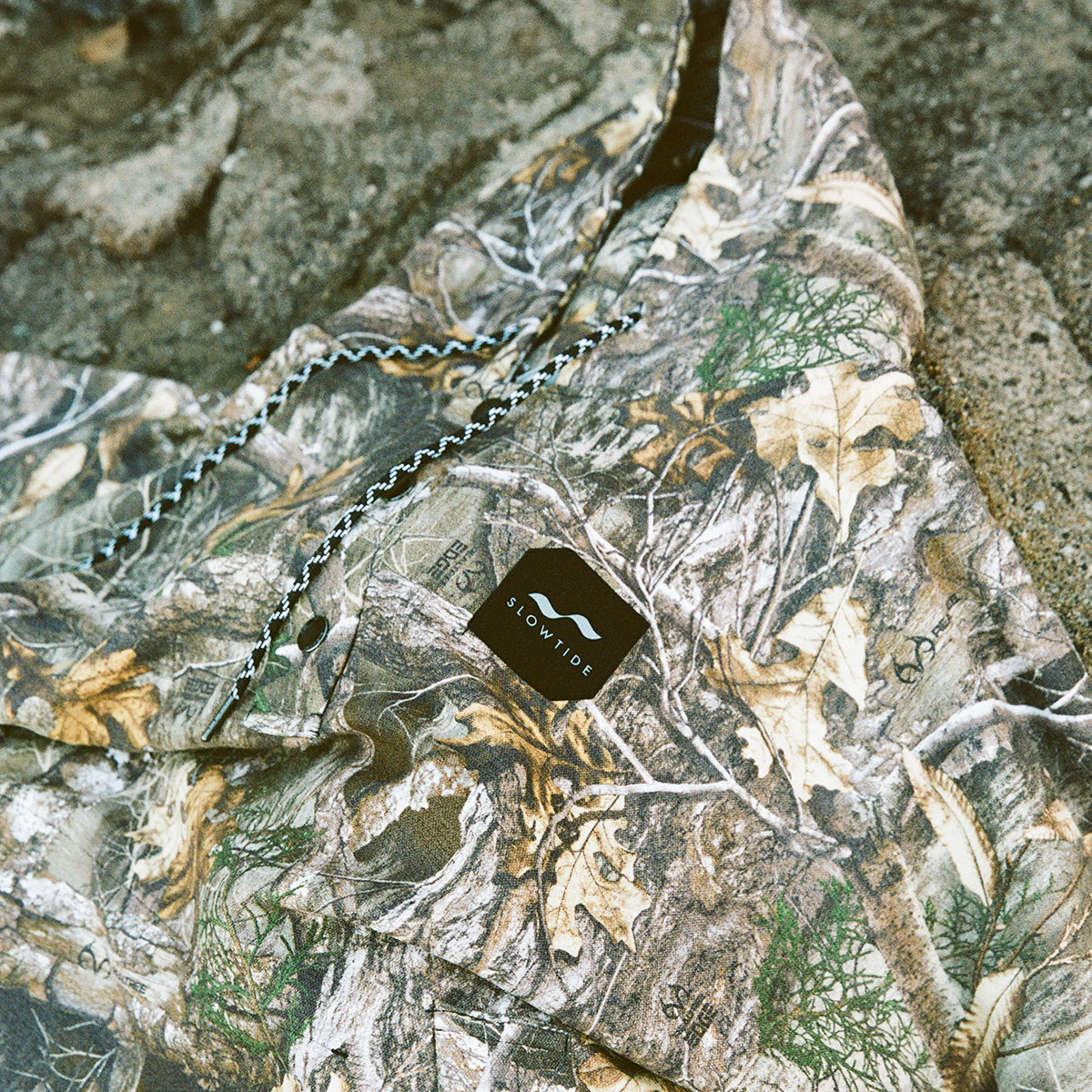 Green camouflage hoodie with black tag on stone surface.