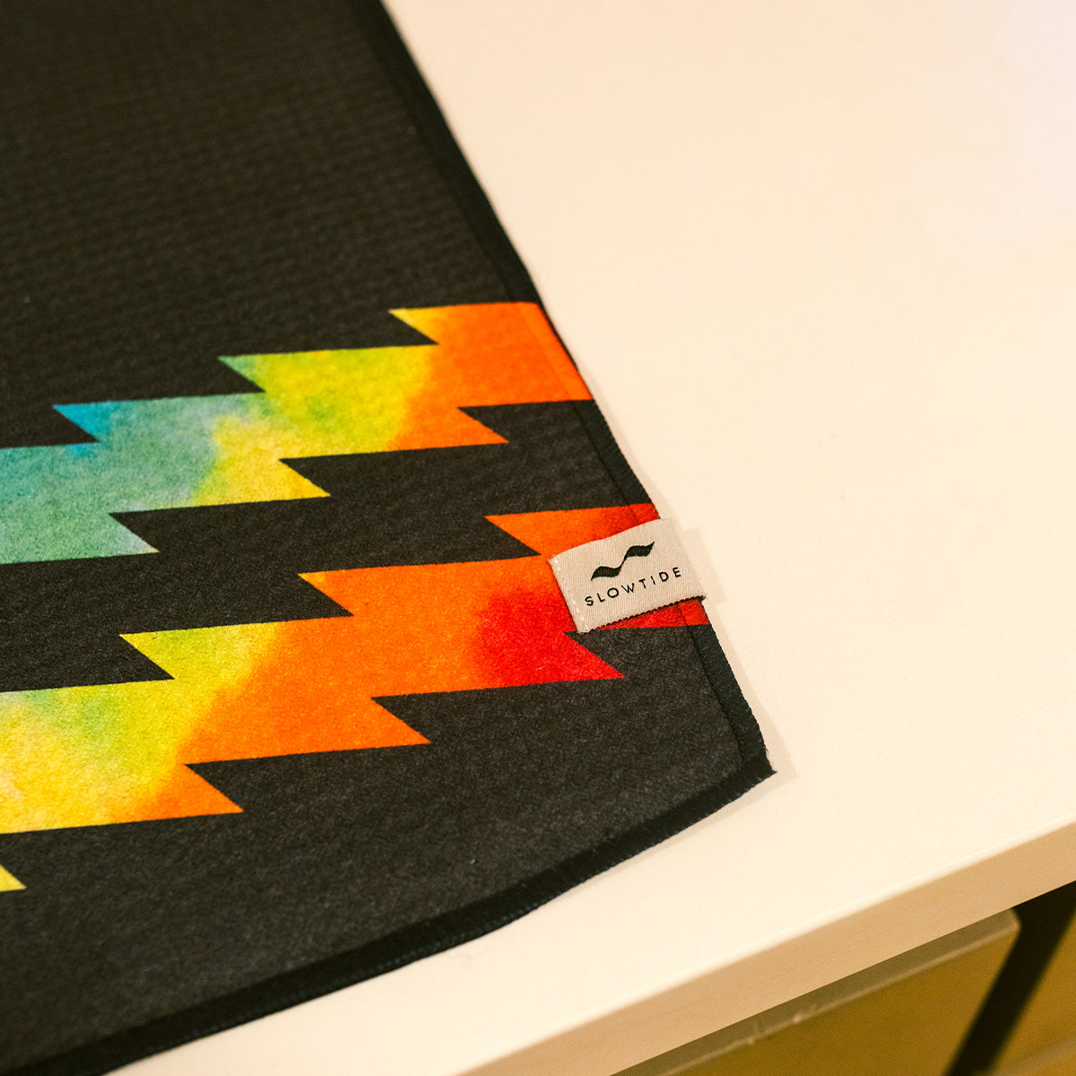 Black quick-dry towel with rainbow lightning bolt pattern on a white surface.