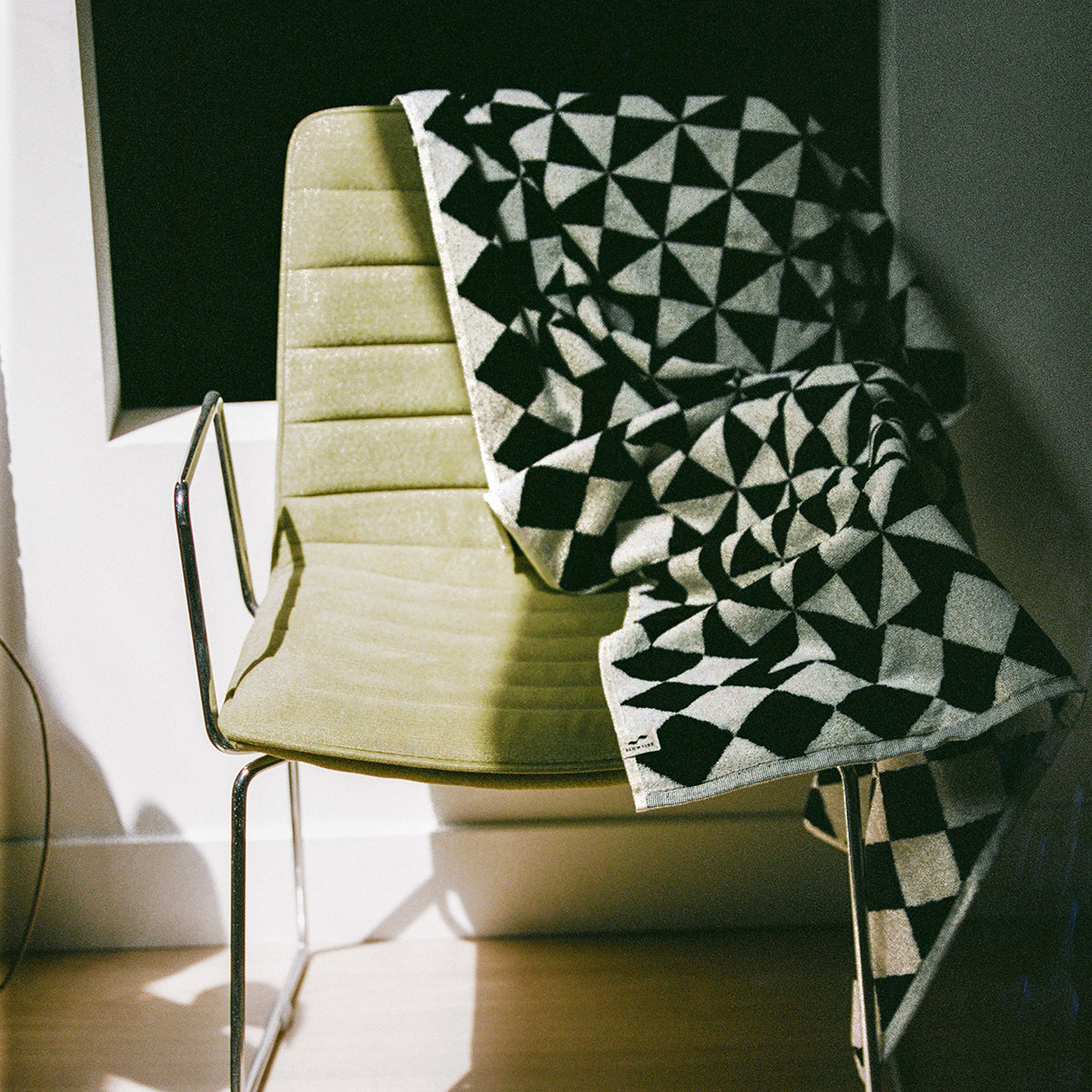 Geometric pattern blanket with bold shapes displayed on a beige chair in natural light.
