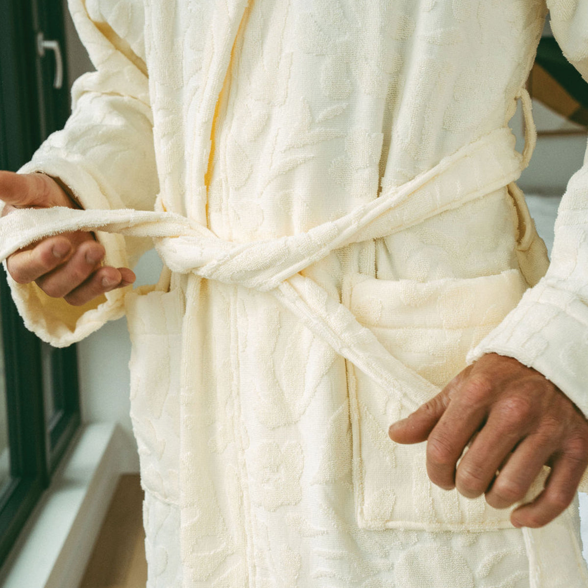 Plush terry cloth robe in cream with embossed floral pattern and tie belt.
