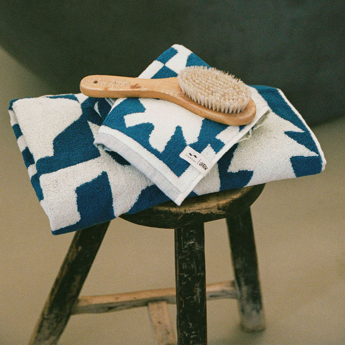 Cotton towels with wooden brush on top, displayed on a rustic wooden stool.