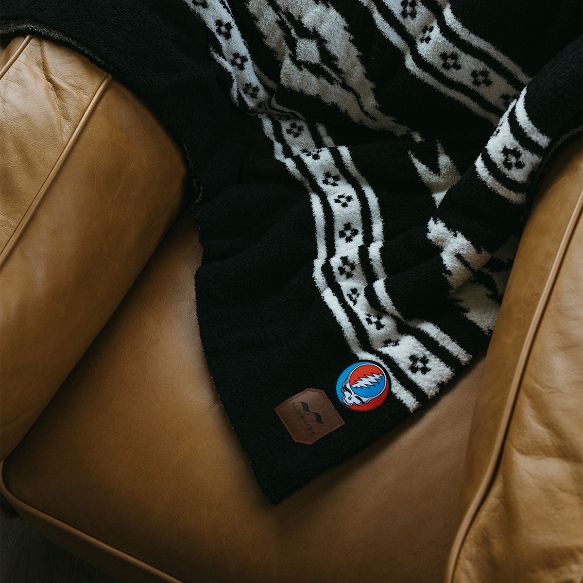 Woven blanket with blue and red patchwork draped over tan leather chair.