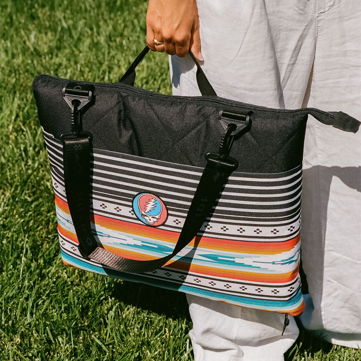Striped tote bag with black handles on grass.
