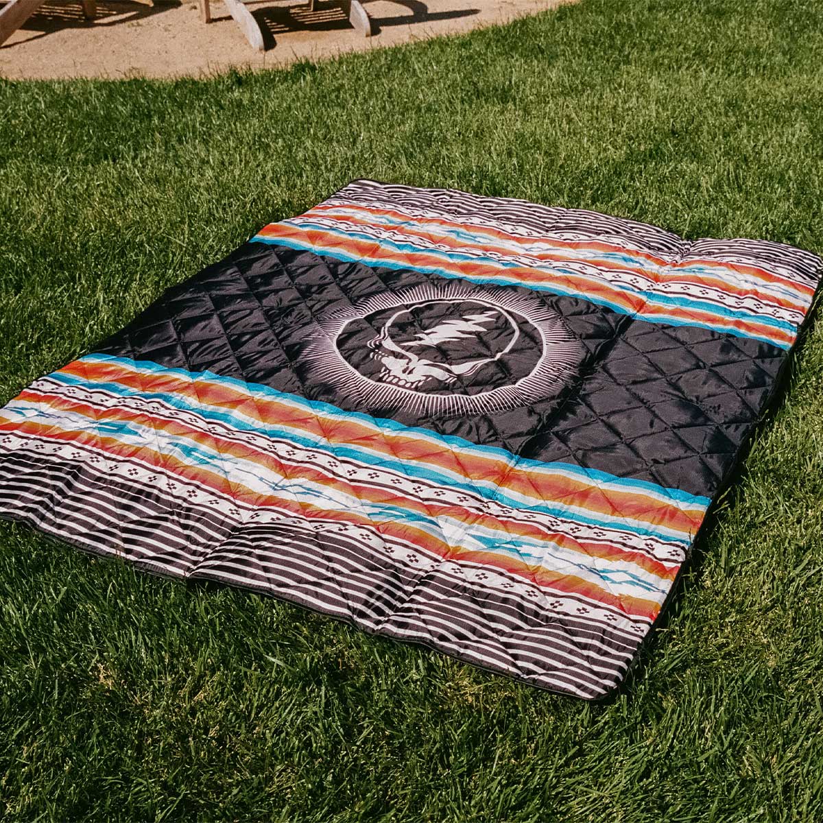 Picnic blanket with face pattern on grass in sunlight.