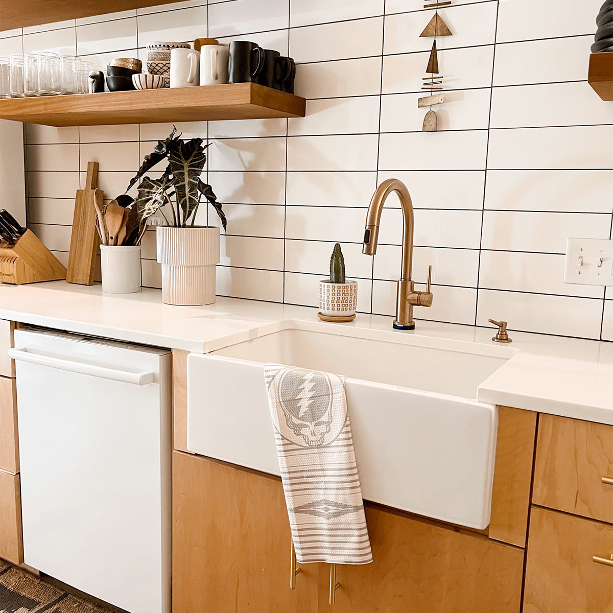Kitchen towel with colorful graphic on open shelf in modern kitchen with farmhouse sink.