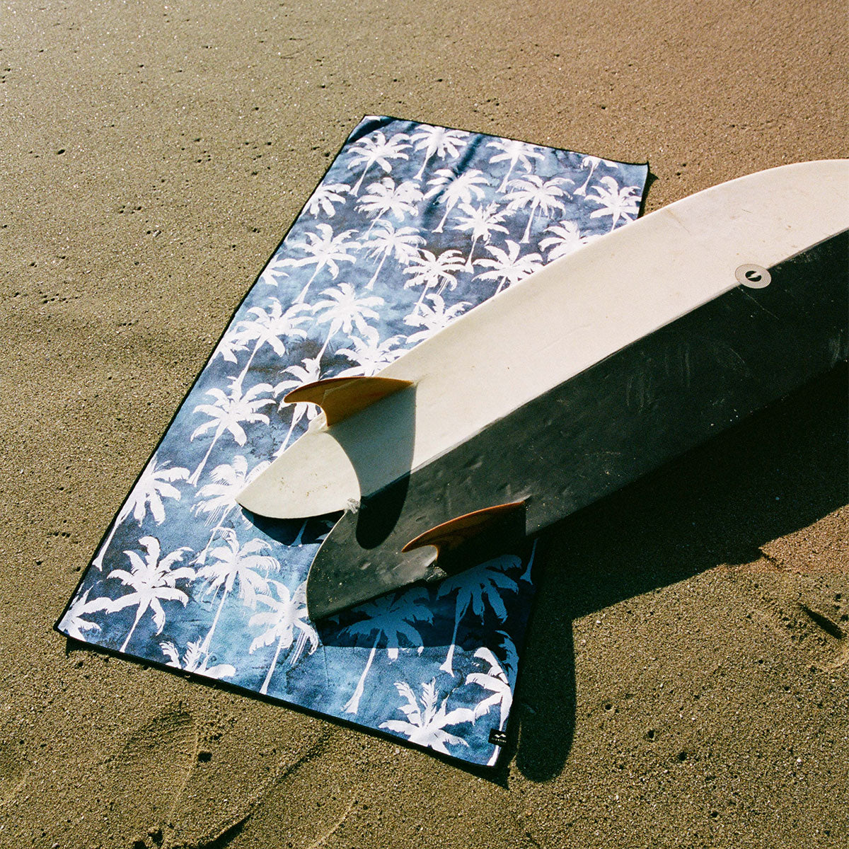 Surfboard on blue tie-dye towel, sandy beach setting.