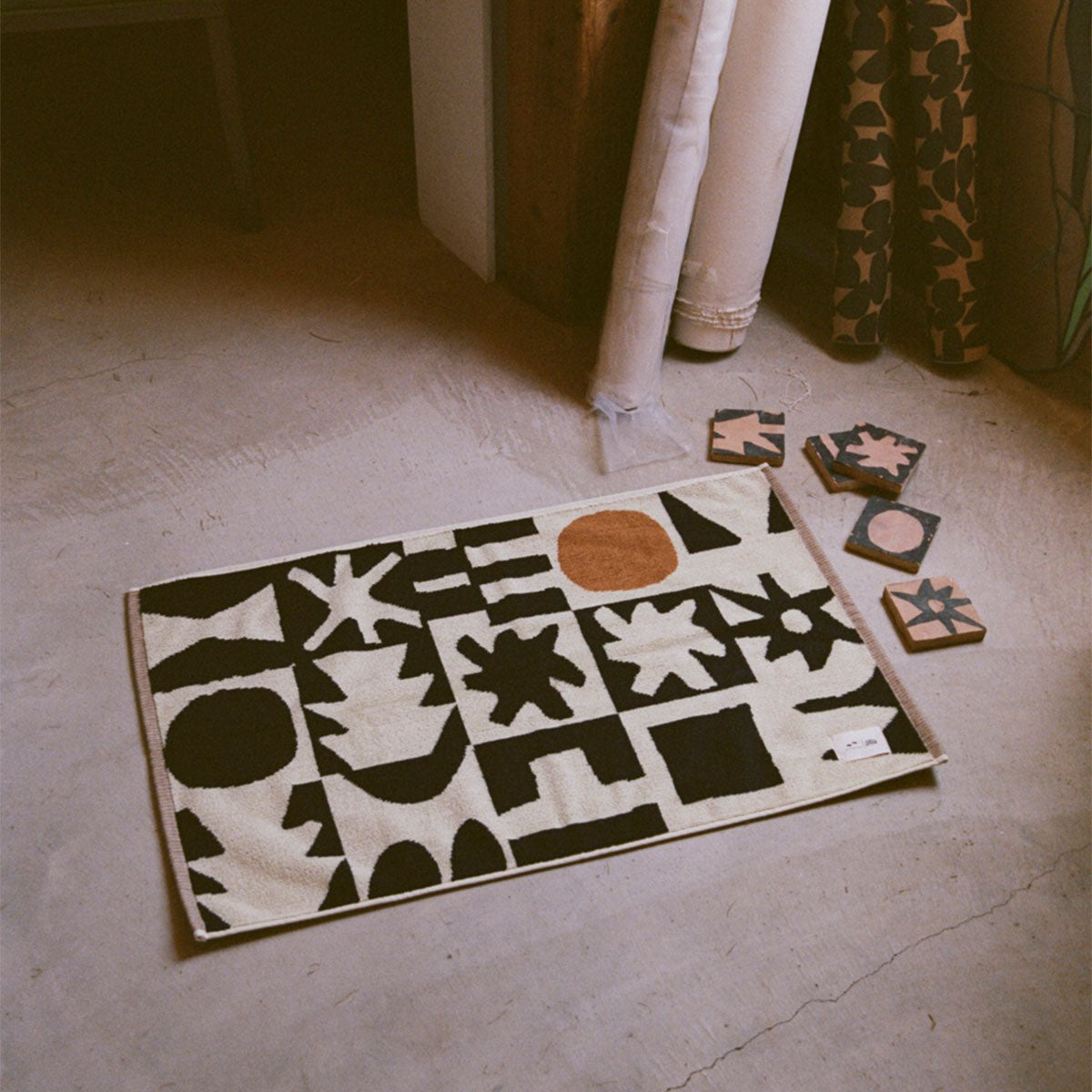 Bath mat, absorbent cream fabric with black abstract shapes and rust circle pattern on floor.