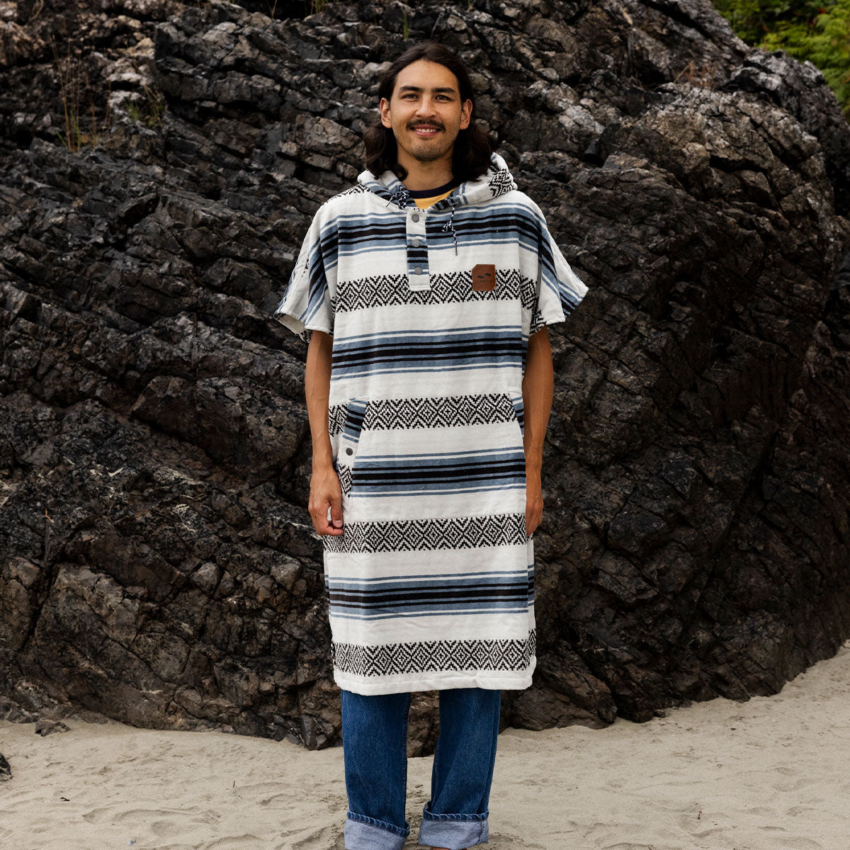 Cotton towel poncho with stripes on sand near rocks.