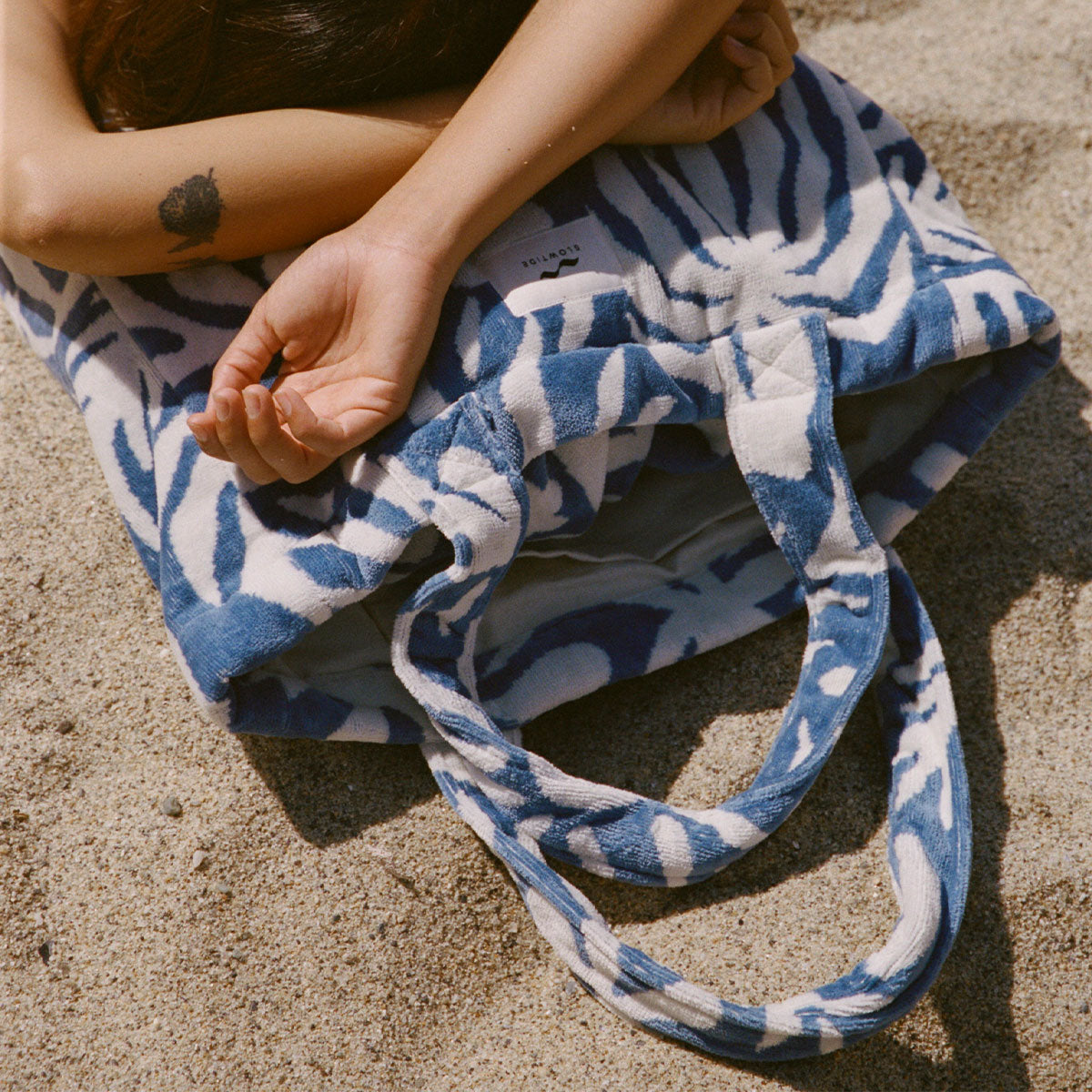 Terry bag with blue and white pattern on sandy ground.