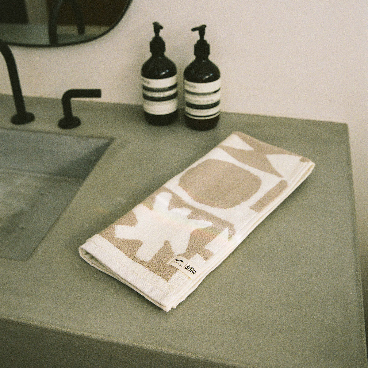 Bath towel, cotton, folded next to soap dispensers on concrete bathroom countertop.