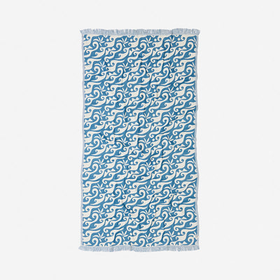 Beach towel with ocean blue swirling wave pattern and fringed edges for beach use.