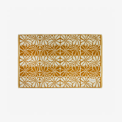 Cotton bath mat with yellow and white geometric floral pattern, small corner label visible.
