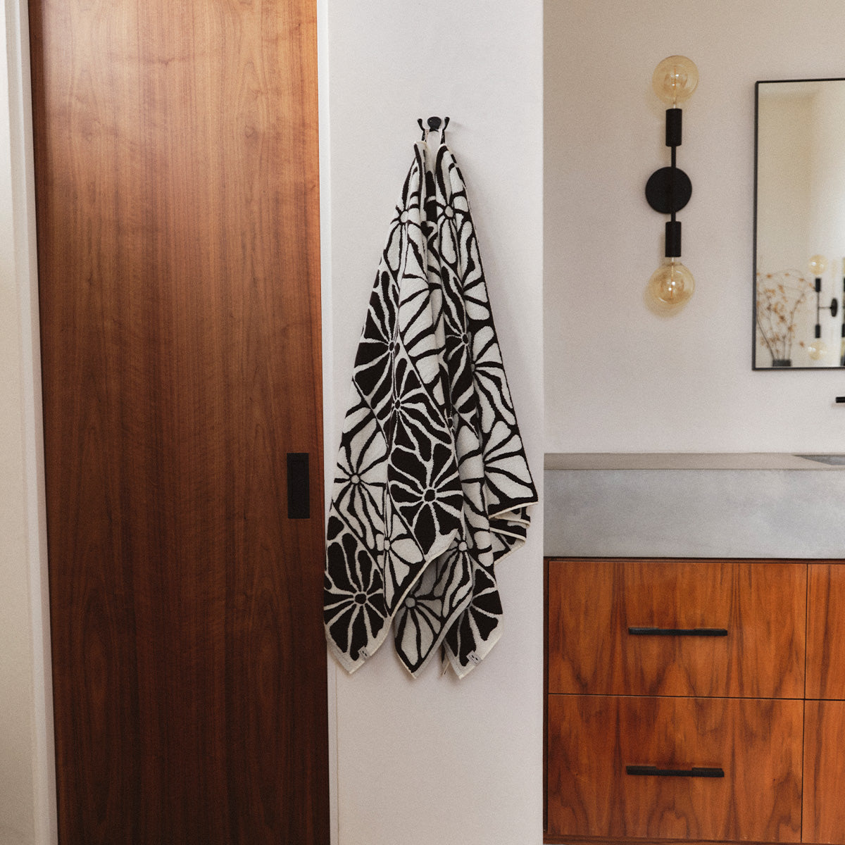 Bath towel with black and white floral stripe pattern hanging on a white wall.