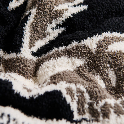 Woven blanket with black, white, and beige geometric patterns for home decor.
