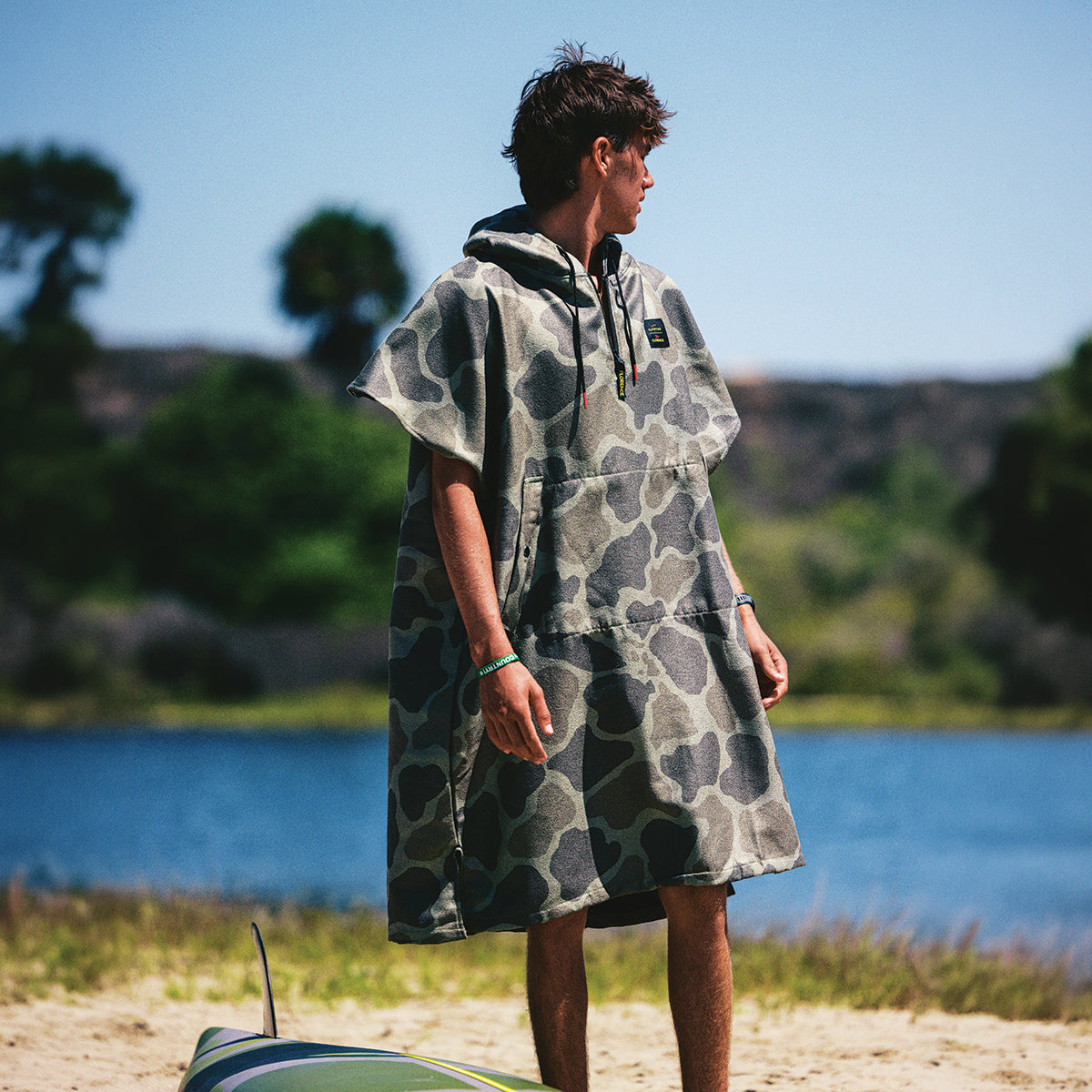 Camo quick-dry poncho with hood, shown outdoors near a lake.