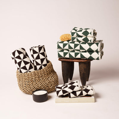 Bath towel with geometric pattern on a stool, candle and sponge in woven basket nearby.