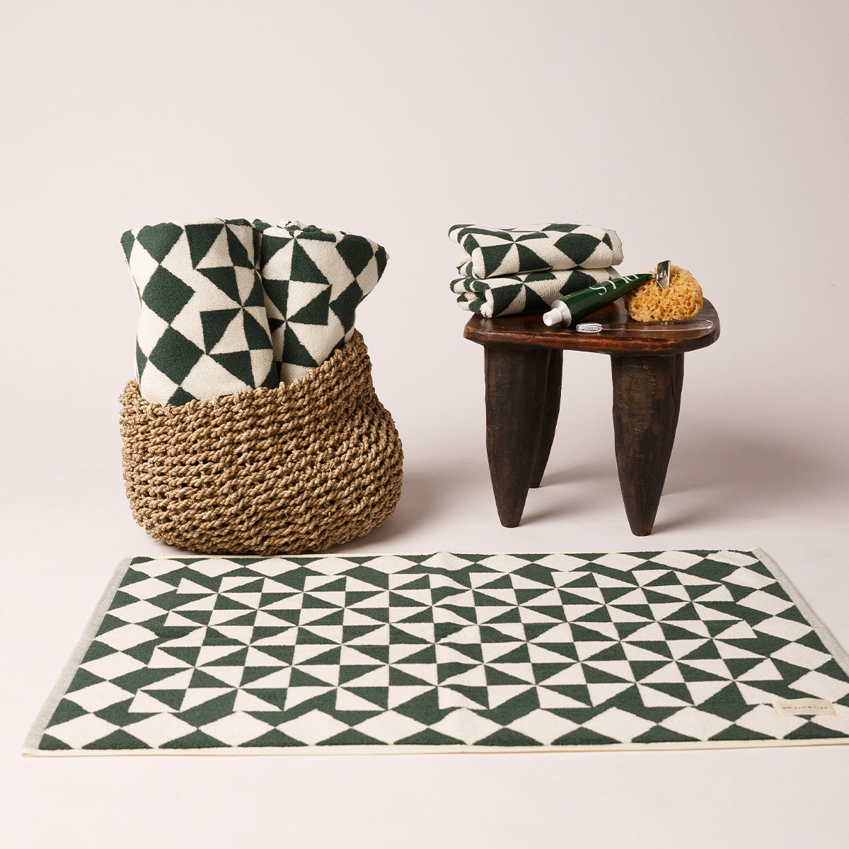 Cotton towels with green and white geometric pattern in basket, shown with absorbent bath mat.