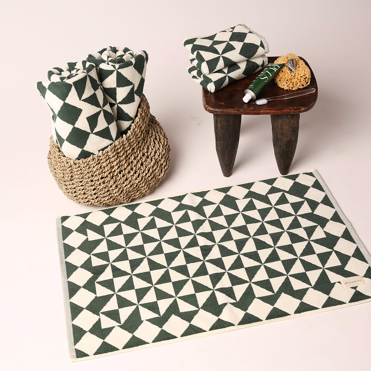 Bath towels with green and white geometric pattern, matching mat, in basket with stool and toiletries.