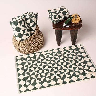 Bath towels with green and white geometric pattern, matching mat, in basket with stool and toiletries.