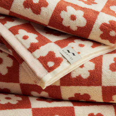 Towel with red and cream floral geometric checks, folded with fabric tag visible.