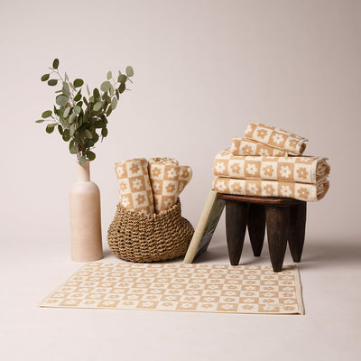 Towel and rug with floral checkerboard pattern in a minimal setting with vase of eucalyptus.