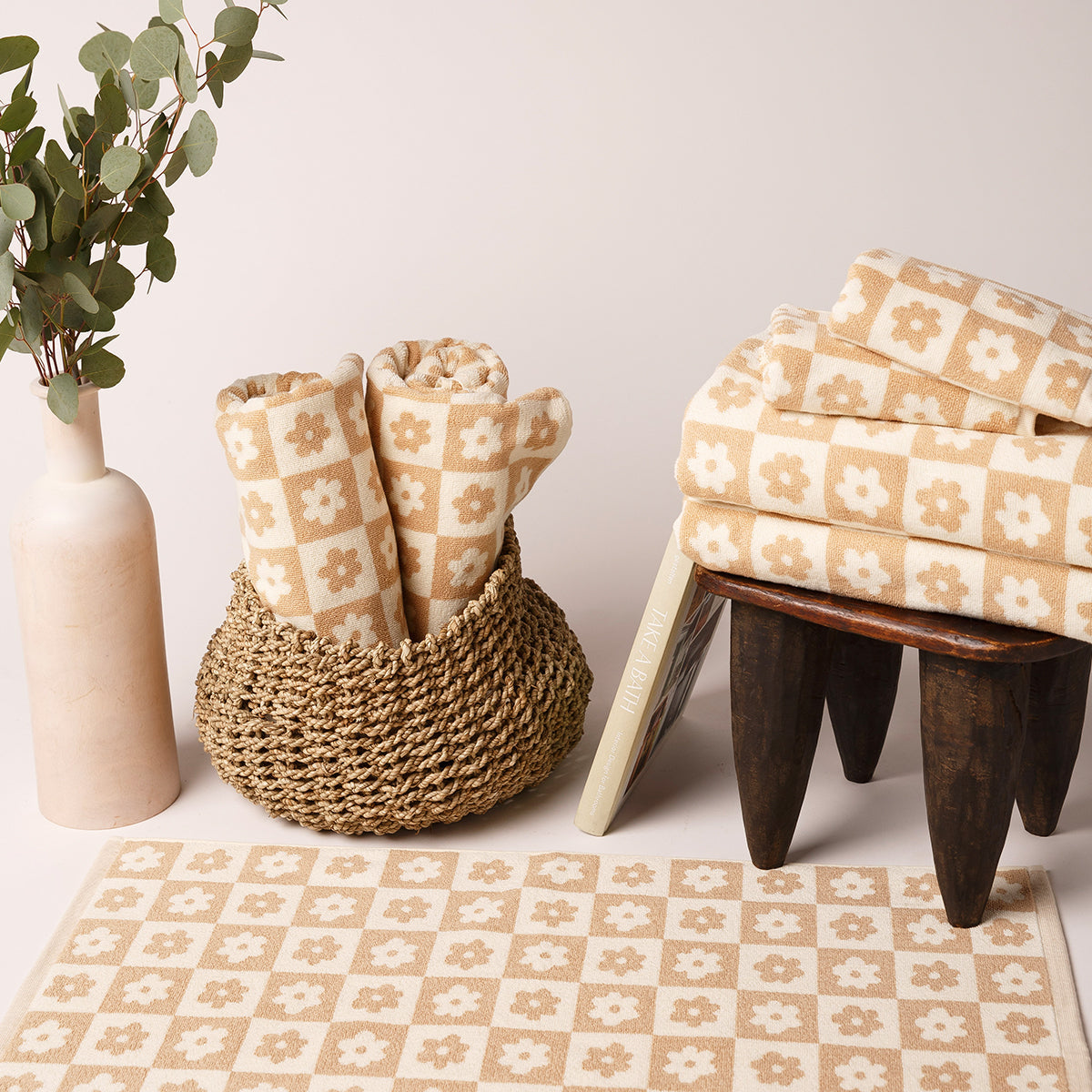 Cotton towels with beige and white floral pattern in a basket and on a stool.