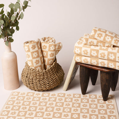 Cotton towels with beige and white floral pattern in a basket and on a stool.