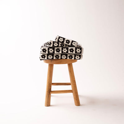Bath towel with black and white floral pattern, folded on a wooden stool.