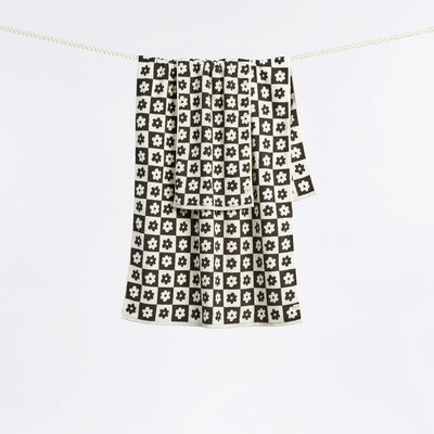 Hand towel in sustainable cotton with black and white check pattern and floral accents on clothesline.