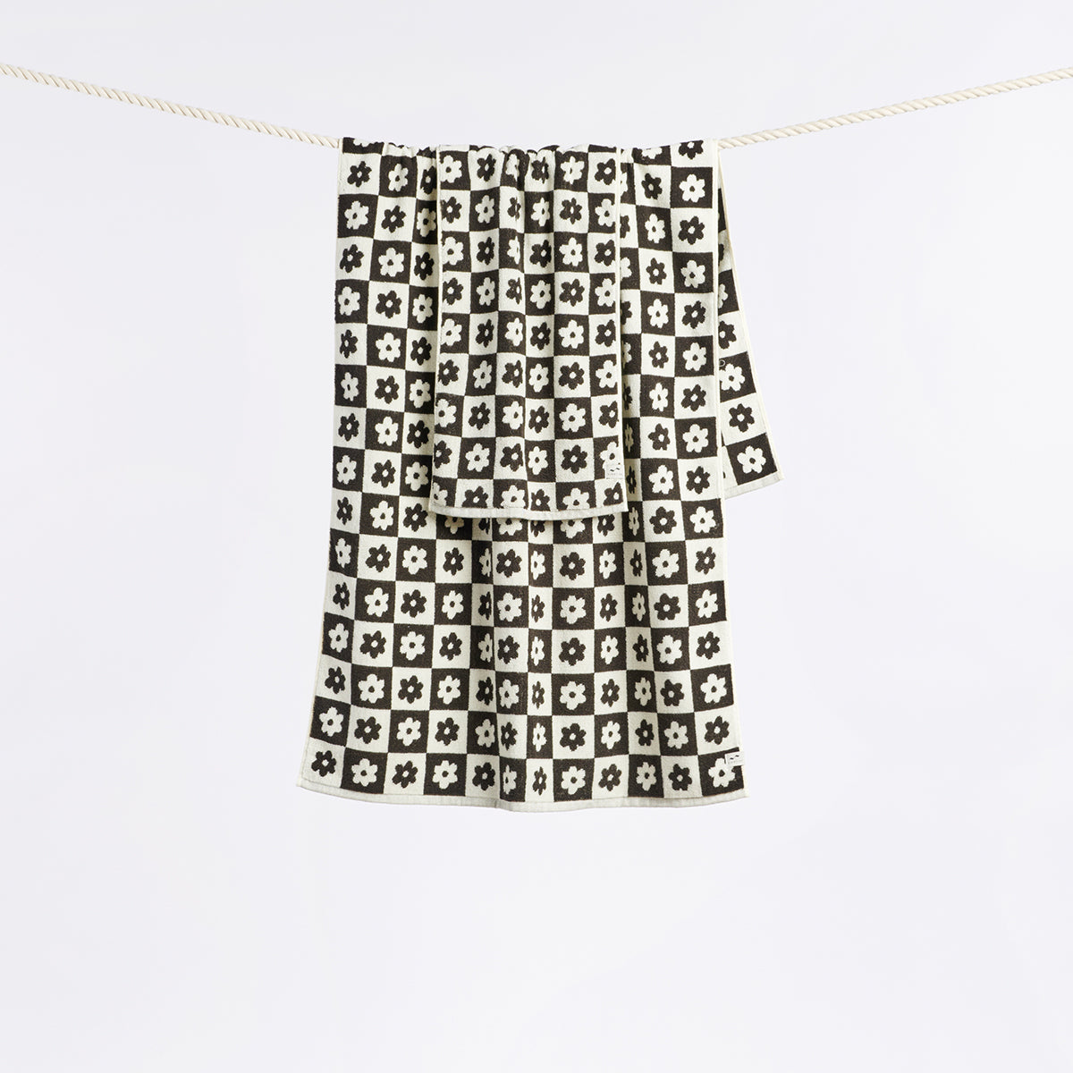 Hand towel in sustainable cotton with black and white check pattern and floral accents on clothesline.