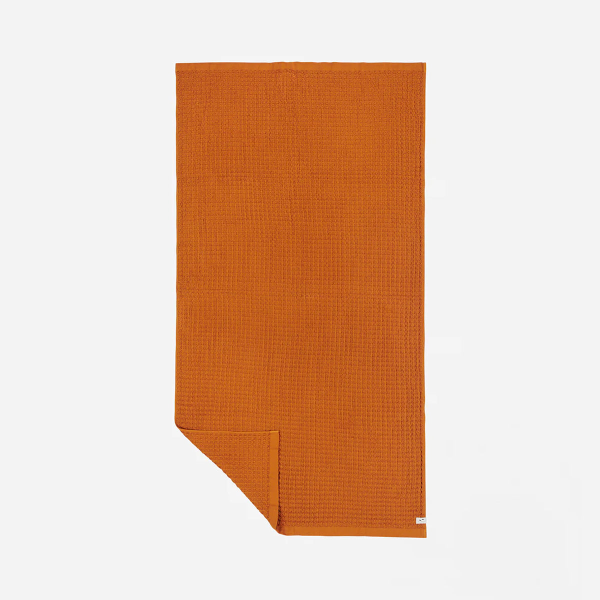 Waffle bath towel in burnt orange with folded corner on white background.
