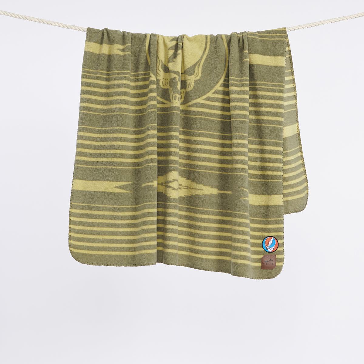 Vintage throw blanket with green and yellow pattern and small corner patch, displayed hanging.
