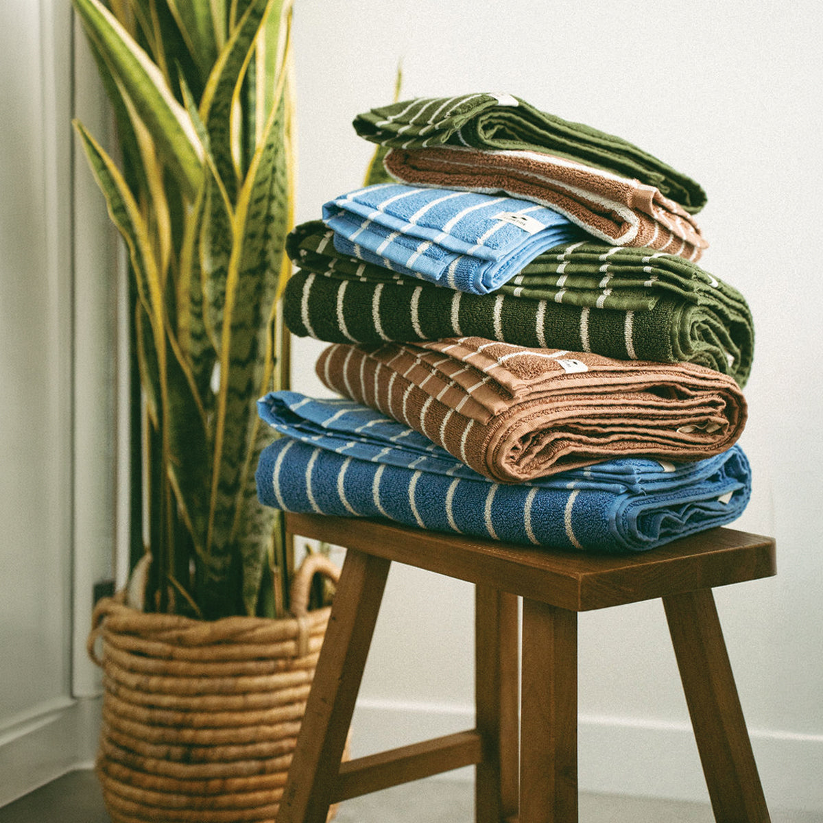 Plush bath towels in blue, green, and brown stripes stacked on a wooden stool.