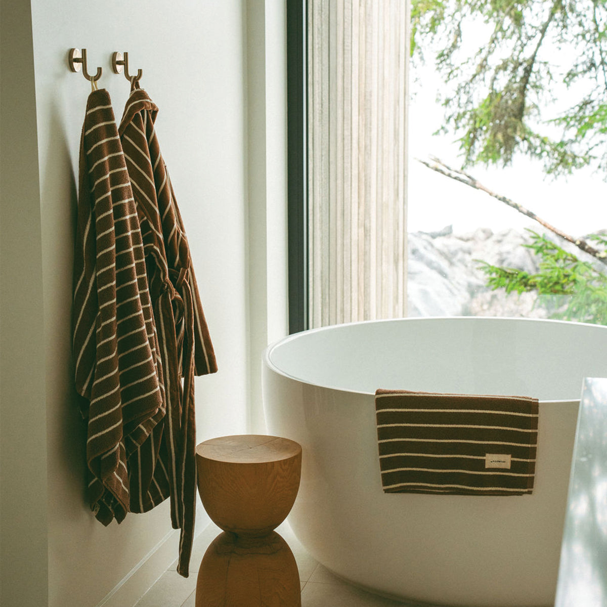 Cotton bathrobe and plush towel bundle with stripes hanging by a tub.