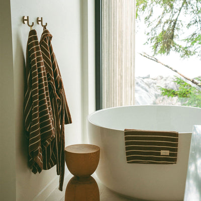 Cotton bathrobe and plush towel bundle with stripes hanging by a tub.
