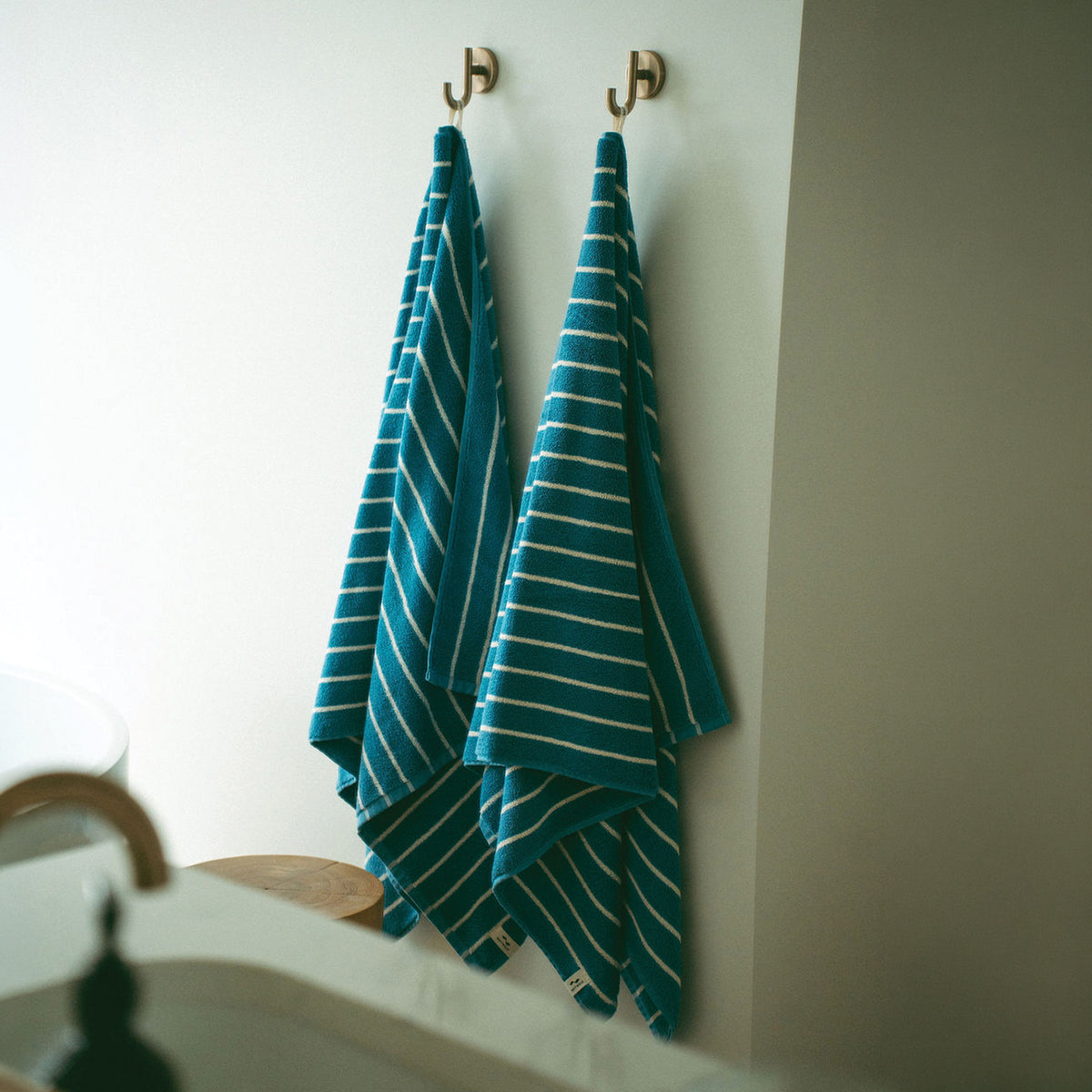 Plush teal striped bath towels hanging on wall hooks.