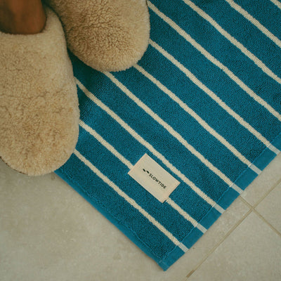 Cotton bath mat with blue and white stripes on a tiled floor.