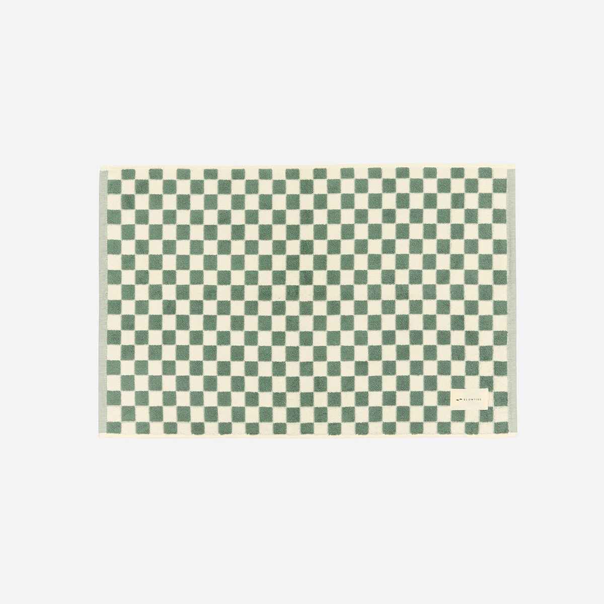 Bath mat with green and cream checkerboard pattern, small label on corner.